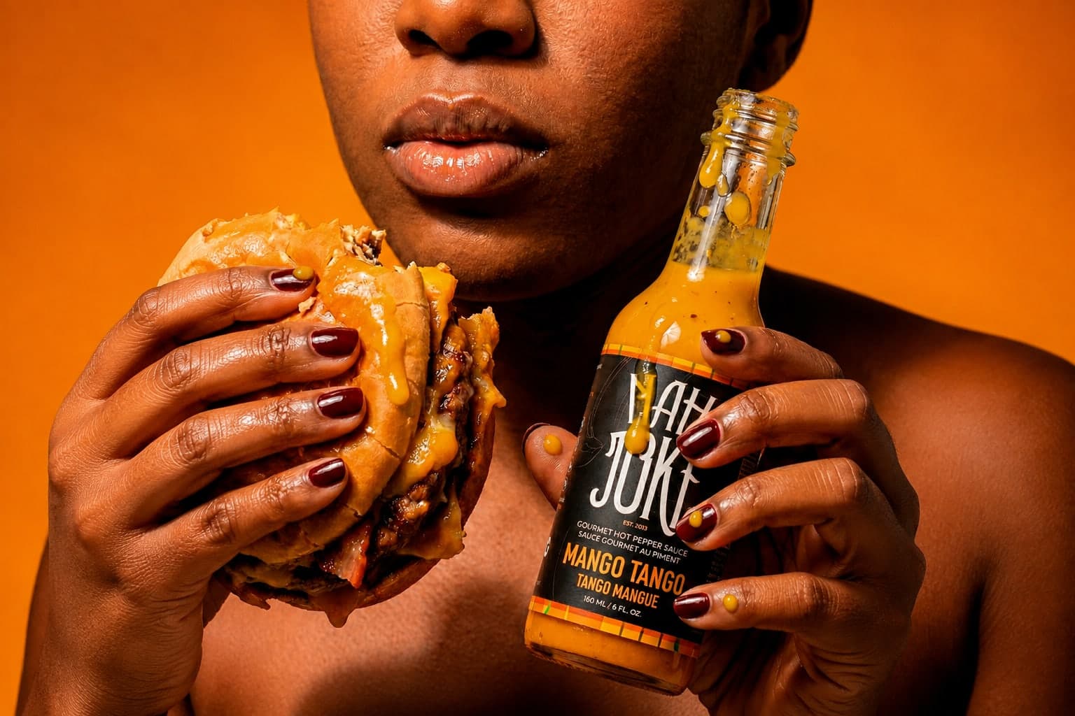 Holding a loaded burger in one hand and a bottle of Nah Joke Mango Tango in the other